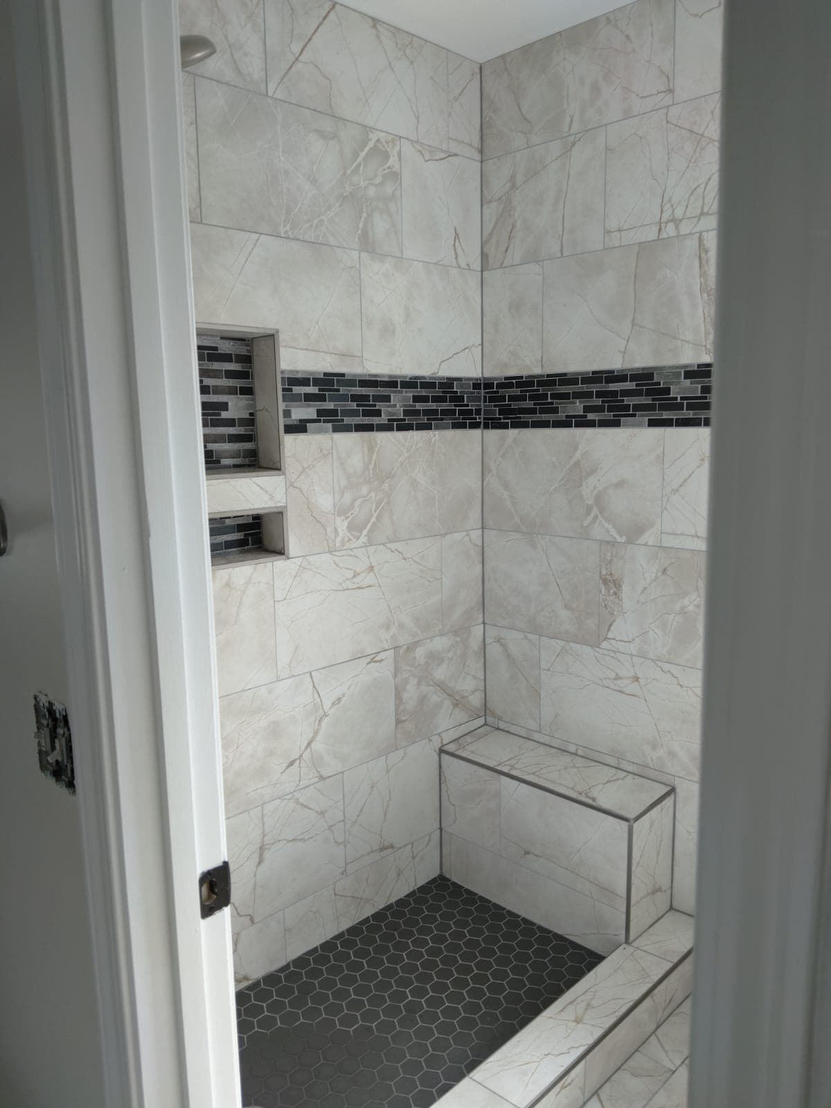 Shower with marble-style tiles and dark floor accent