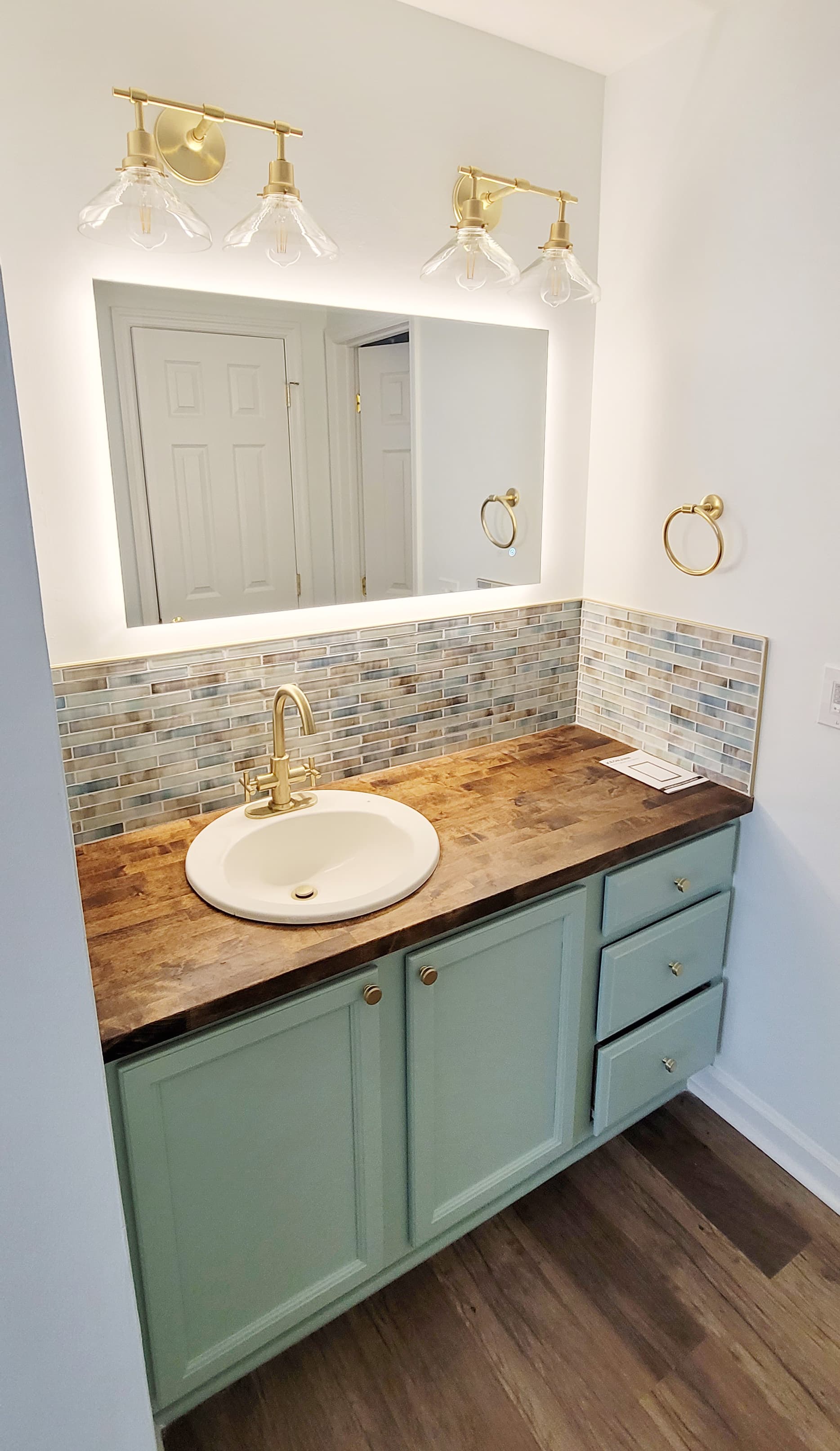Updated bathroom vanity with wood countertop, backsplash, and brass lighting